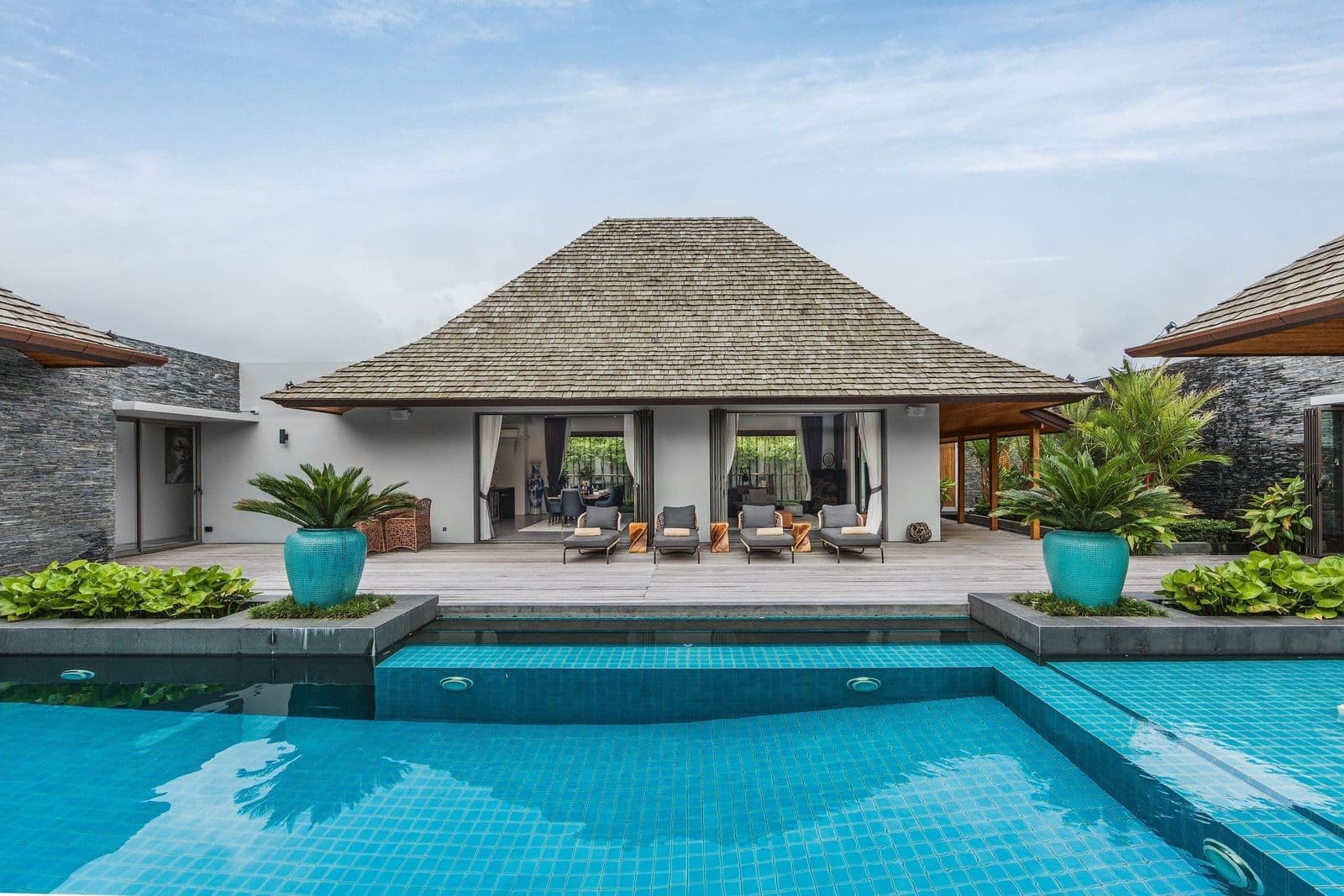 Balinese-style pool villa with shingle roof, sun deck and loungers beside a turquoise swimming pool in Layan, Phuket.