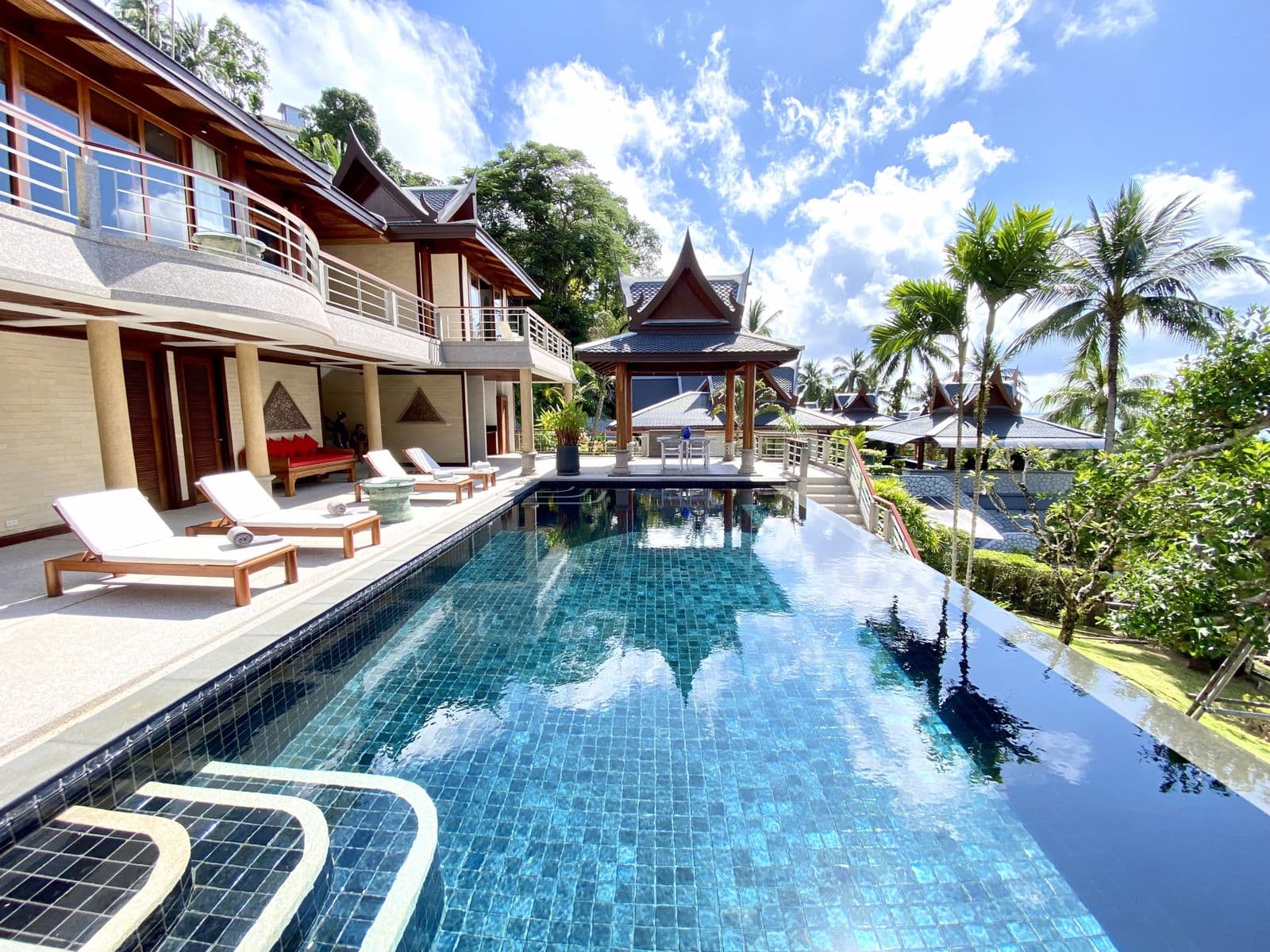 Infinity-edge pool with sun loungers and Thai-style pavilions at a villa in Phuket.